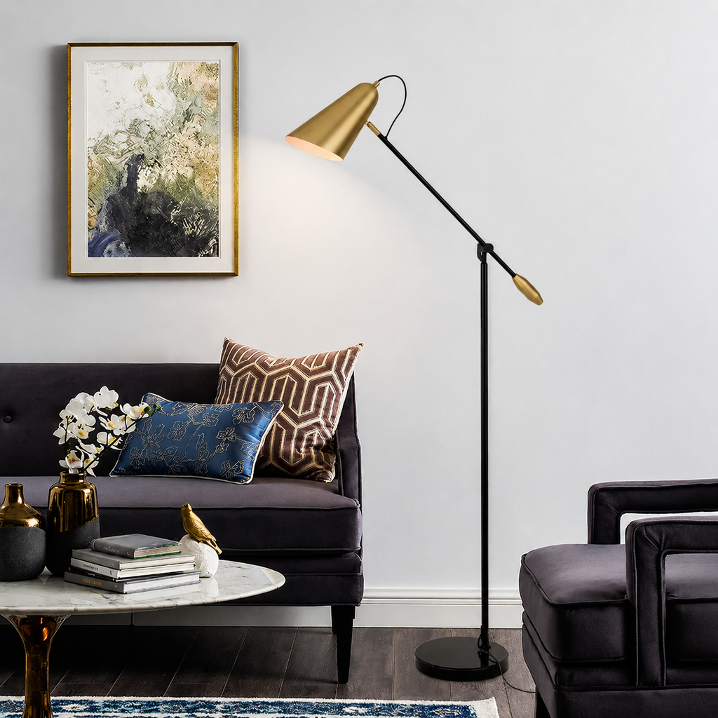 A modern black floor lamp with a gold conical shade and adjustable arm stands in a styled living room next to a dark purple sofa and a marble coffee table.