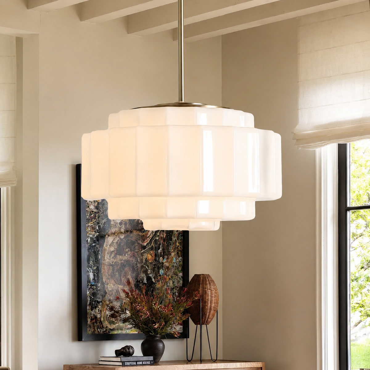 A modern multi-tiered pendant light with a frosted white glass or acrylic shade and a brushed brass or gold-toned metal top canopy and rod, hanging in a styled interior room with a window, artwork, and decor.