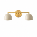 A modern two-light wall sconce with a brushed brass horizontal bar and circular wall mount, featuring two dome-shaped off-white shades, shown against a plain white background.