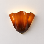 A vintage-style amber glass wall sconce with a wavy, flared shade, mounted on a plain off-white wall and casting a warm light upward.