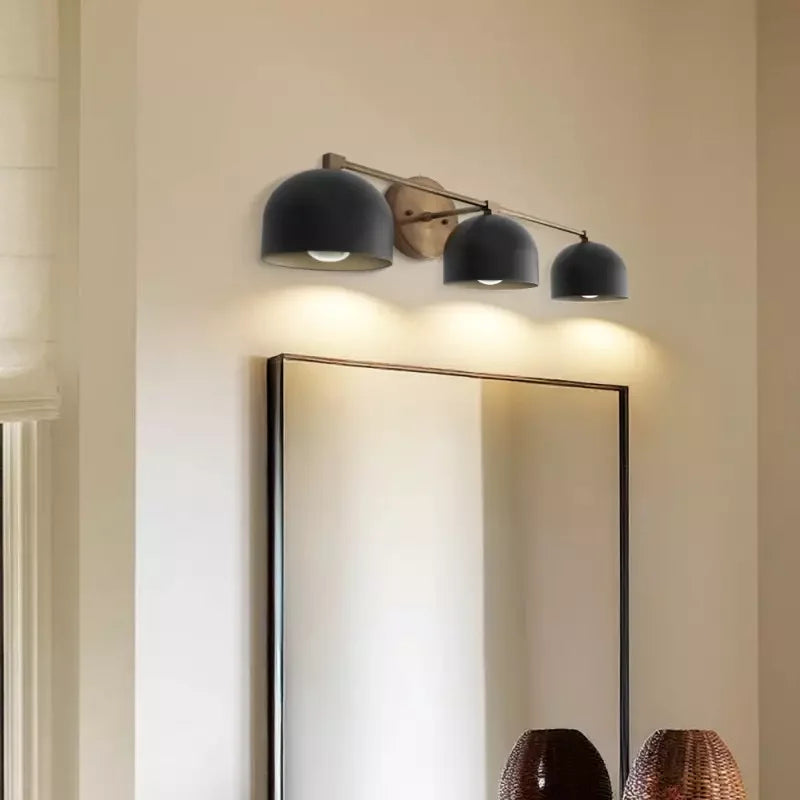 Modern wall light fixture with three black lampshades above a mirror in a room.